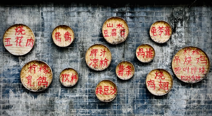Chinese food menu items on bamboo plates on a wall