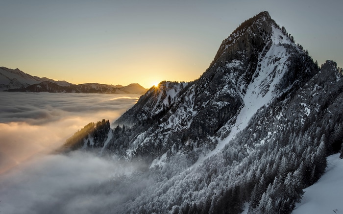 4K snowy mountain peak above clouds at sunrise