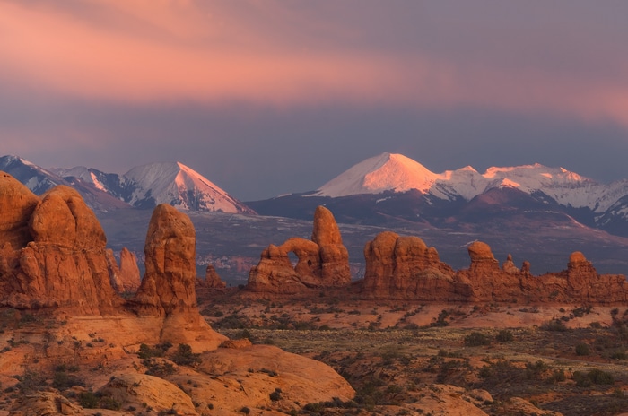 Desert rock formations with snow-capped mountains at sunrise