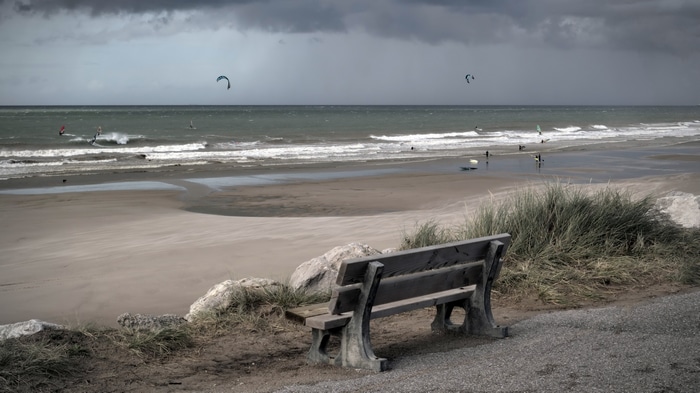 Beach with kite surfers and a bench