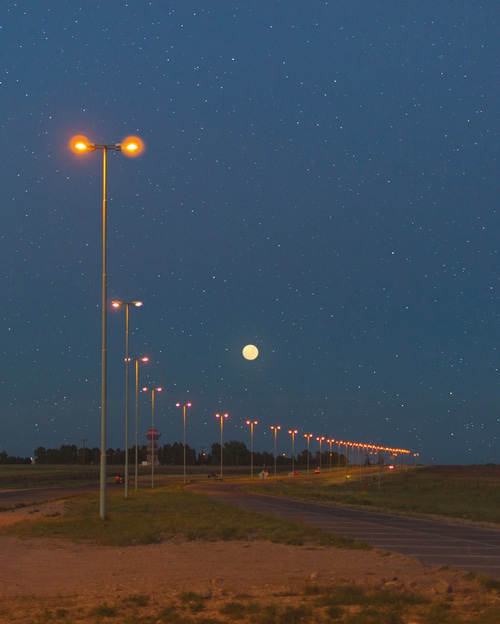 Street lights and the moon under a starry night sky