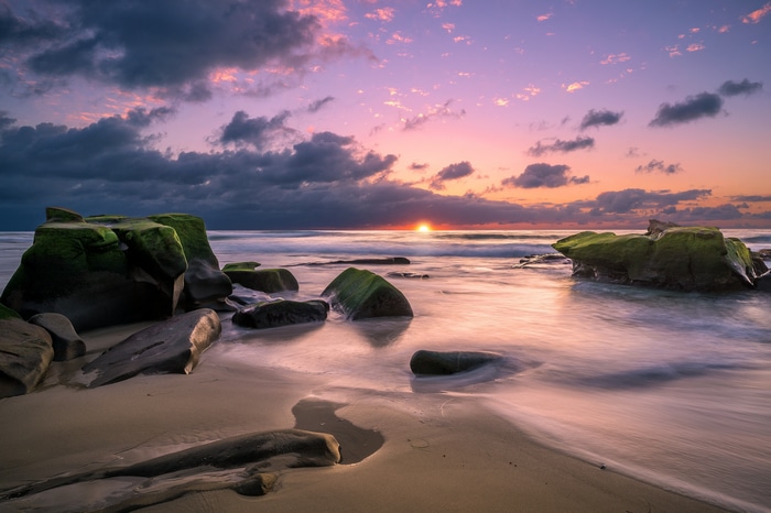 Sunset over the ocean with mossy rocks on the beach
