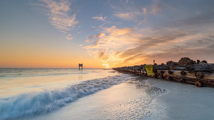 Beach sunset with wooden jetty and sign
