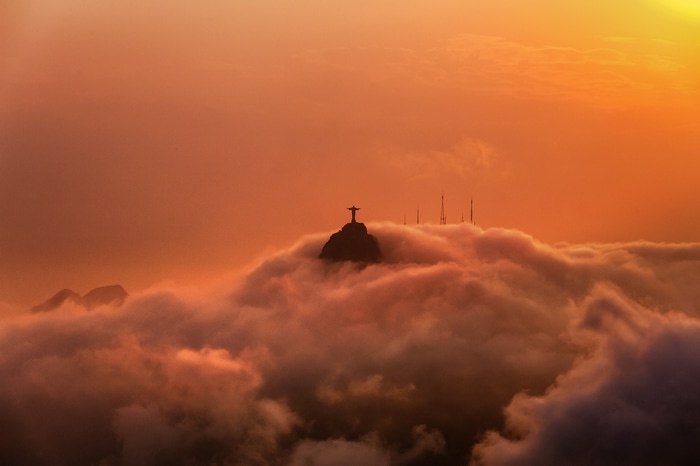 Christ the Redeemer statue above clouds at sunset