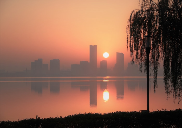 Sunrise over a misty city skyline reflected in a lake