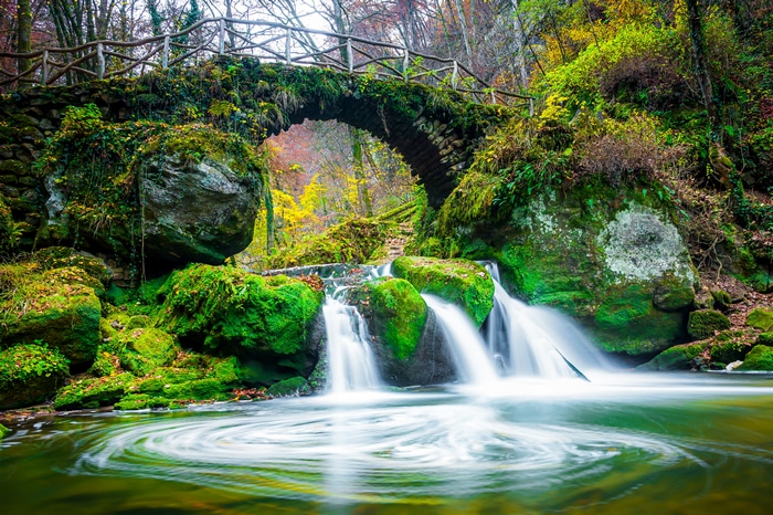 Moss-covered stone bridge over a waterfall in Luxembourg