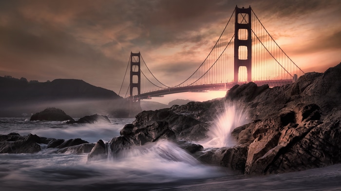 Golden Gate Bridge with waves crashing on rocks