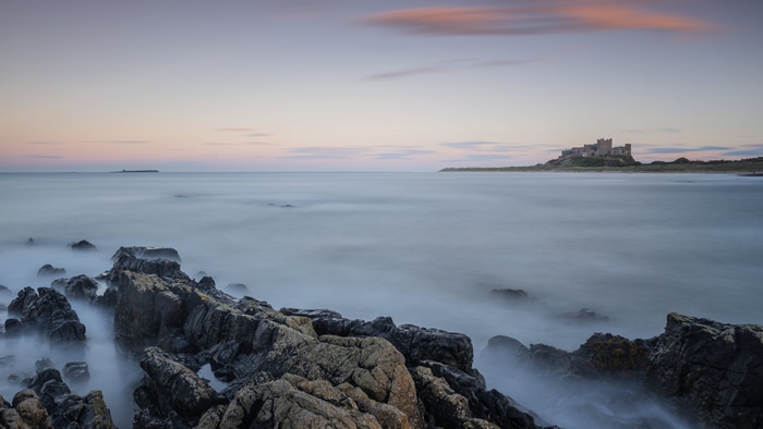 Bamburgh Castle on a rocky coast at dusk