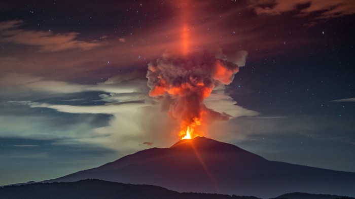 Mount Etna erupting at night with a light pillar