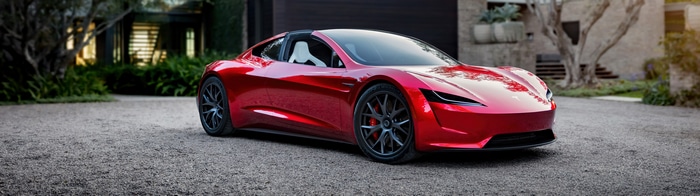 Red Tesla Roadster parked on gravel