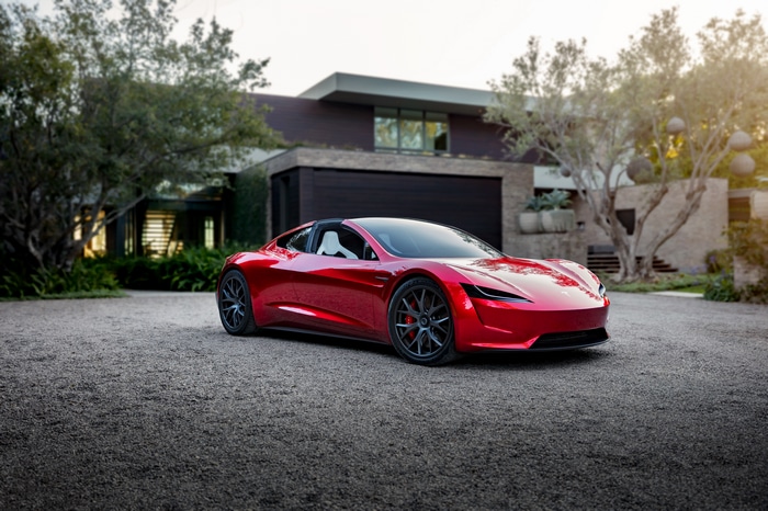 Red Tesla Roadster parked in front of a modern house