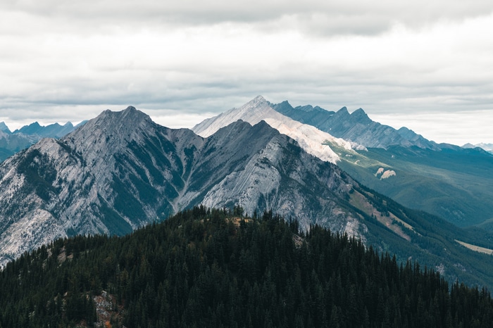 Dark green forest in front of majestic mountains under cloudy sky