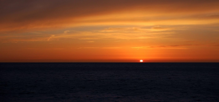 Sunset over the dark ocean with orange clouds