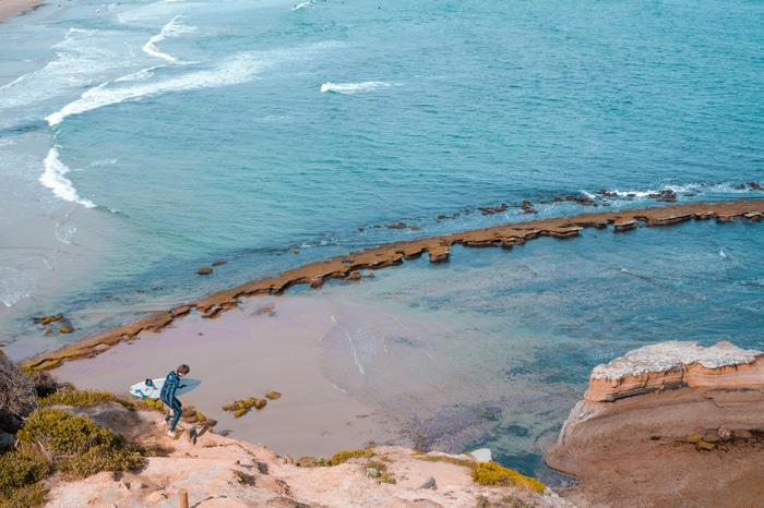 Surfer walking down a cliff with surfboard