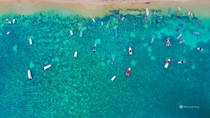 Boats anchored in clear turquoise water near a sandy beach