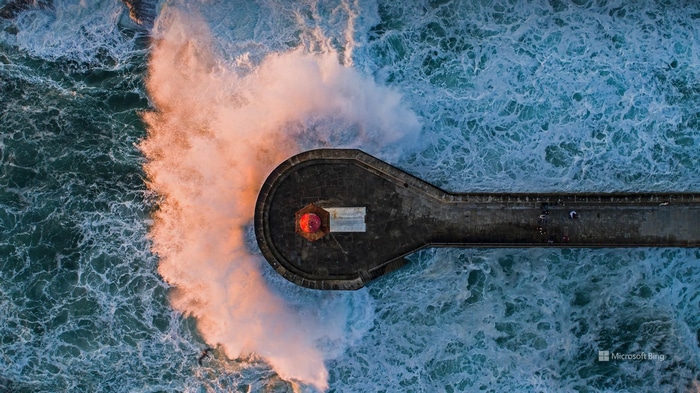Aerial view of a lighthouse during a wave crash