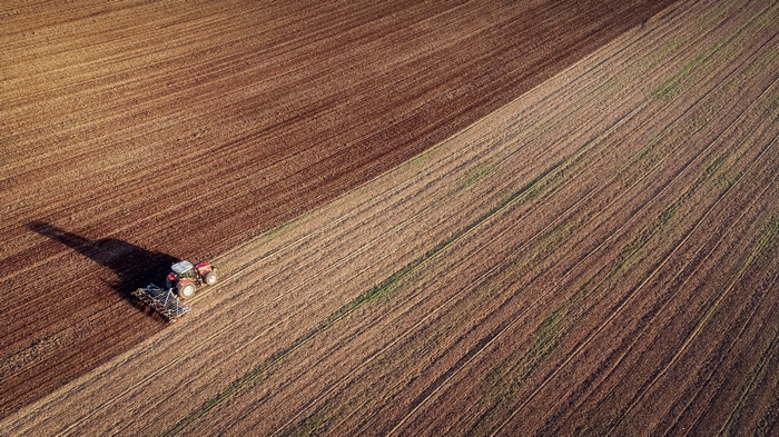 Tractor plowing a large agricultural field from above