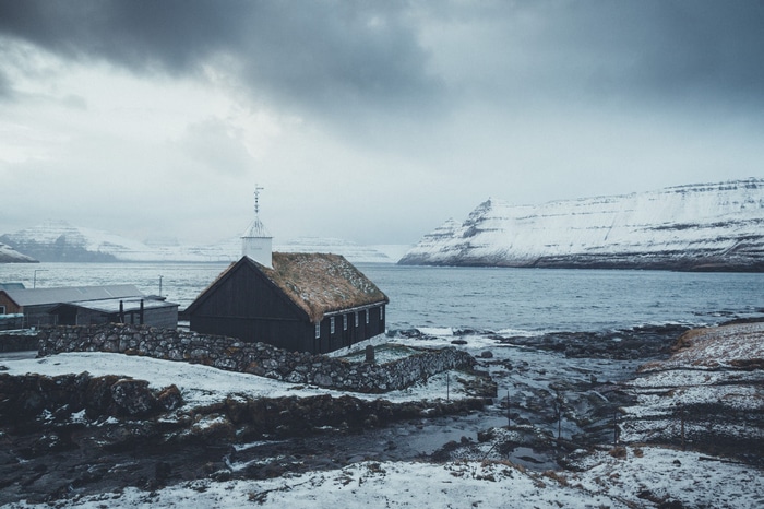 Dark church with grass roof in a snowy village by the sea