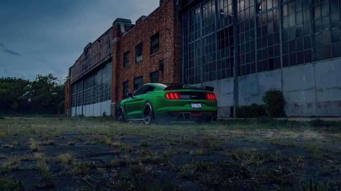 Green Ford Mustang GT350 parked near an old brick building