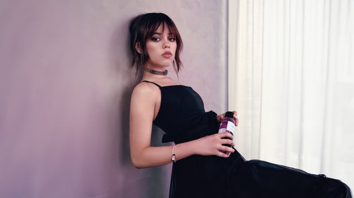 Jenna Ortega in a black dress holding a bottle