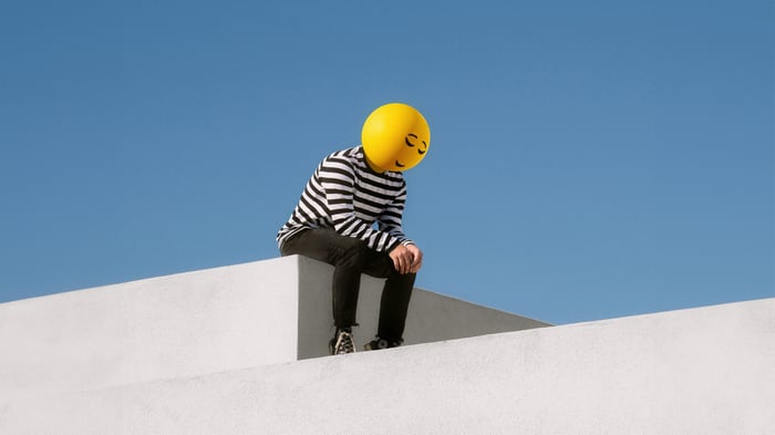 Person with smiley face balloon head sitting on white structure