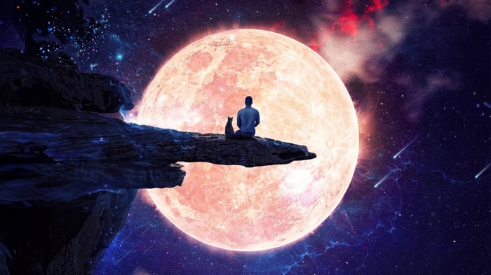 Man and cat sit on cliff overlooking giant moon