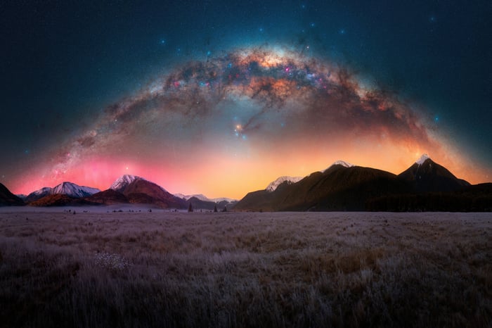 Milky Way Arching Over Mountains and Grassy Field