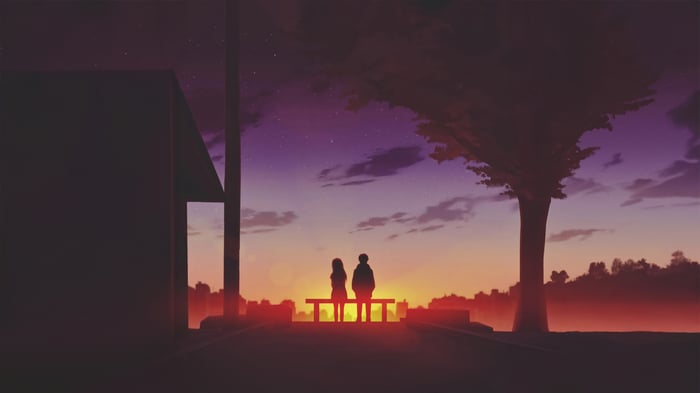 Two figures sit on a bench at sunset