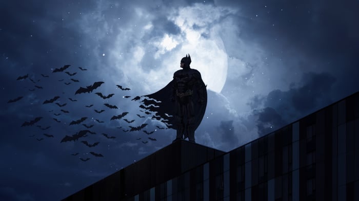 Batman standing on a building with bats flying