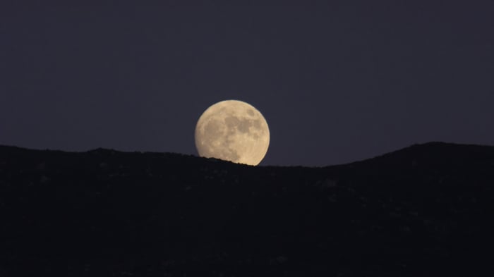 Full moon rising behind dark mountains