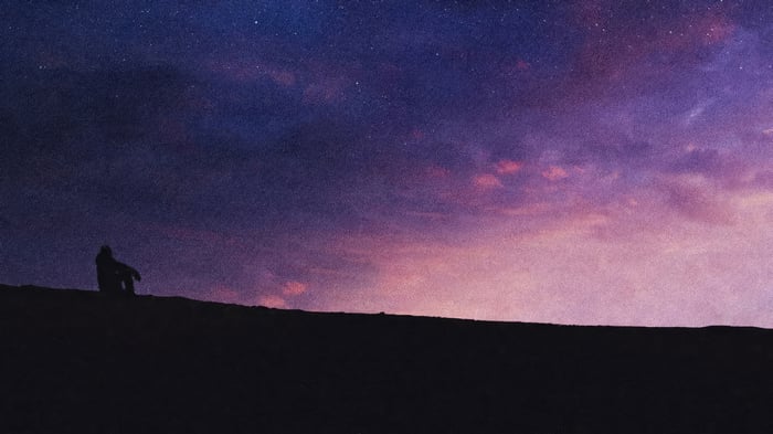 Person sitting on a hill under a starry sky