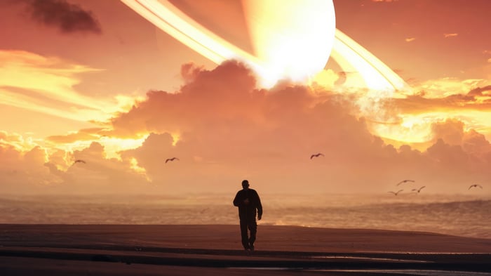 Man walks on beach with Saturn-like planet in sky