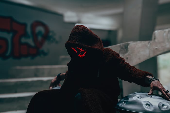 Person in a hooded robe with a glowing mask and a handpan