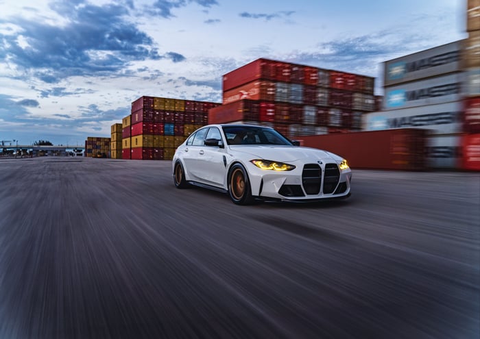 White BMW G80 M3 driving past shipping containers