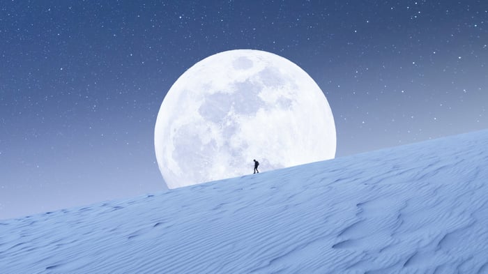 Person walking on sand dune towards giant moon