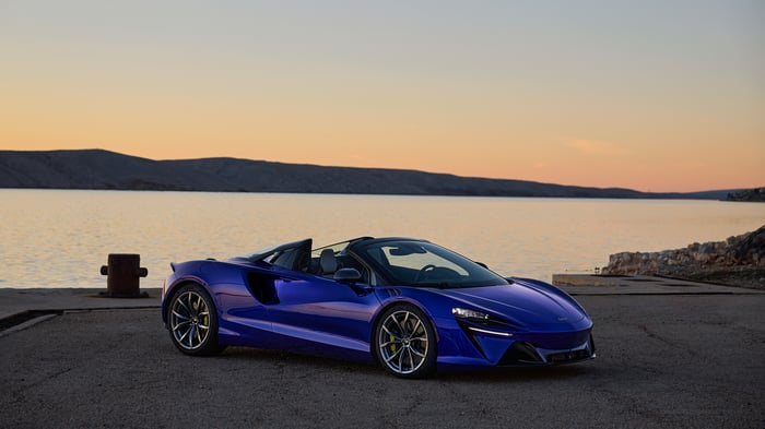 Blue McLaren Artura Spider convertible by the water at sunset