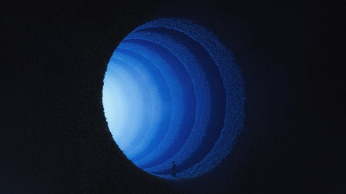 A person stands at the entrance of a blue glowing tunnel