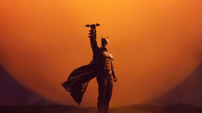 Batman holding a Batarang against an orange sky