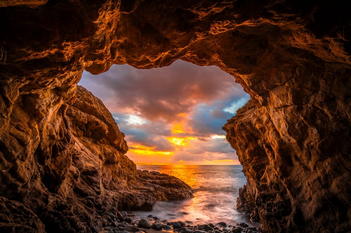 Cave entrance overlooking a sunset over the ocean
