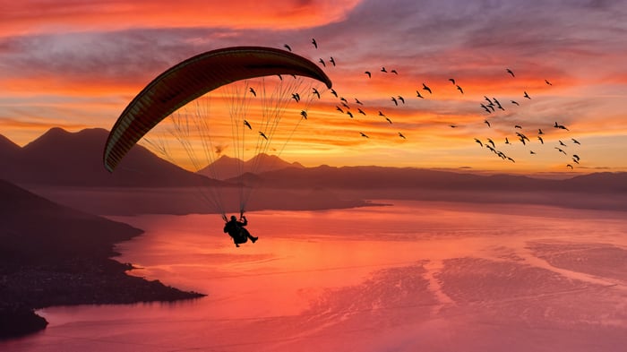Paraglider flying over a lake at sunset with birds