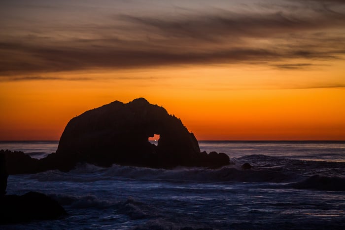 Sunset over the ocean with a rock arch