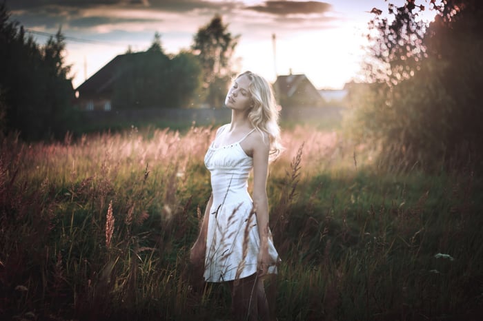 Woman in white dress standing in a field at sunset