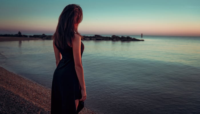 Girl in black dress by the sea at sunset