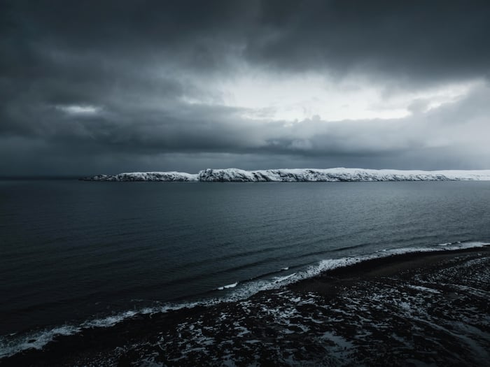 Dark Ocean and Snow-Covered Island Under Stormy Sky