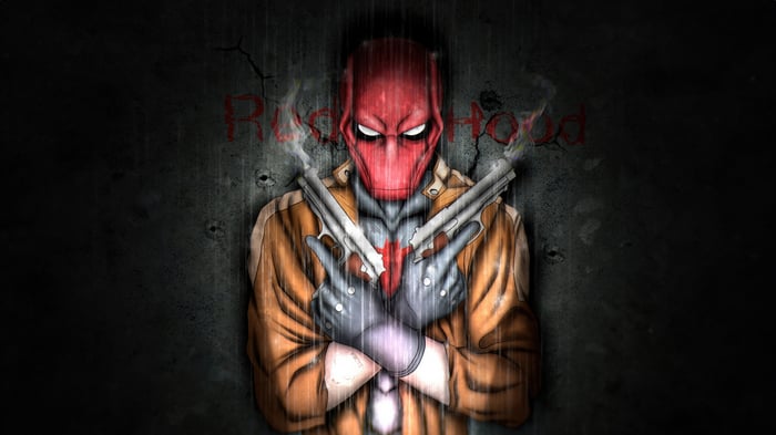 Red Hood holding two guns in front of a concrete wall