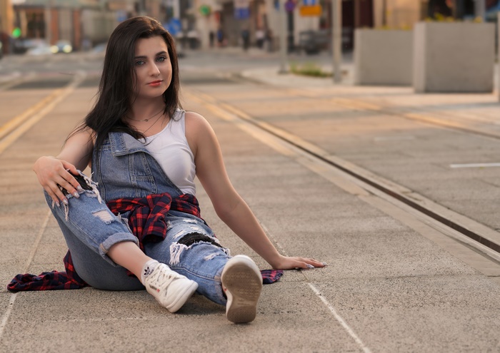 Brunette woman in overalls sitting on tram tracks