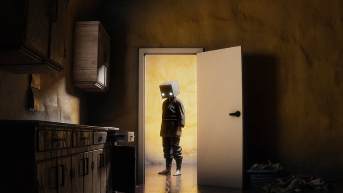 A figure with a box head and glowing eyes stands in a doorway