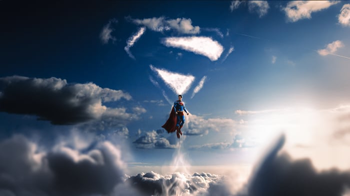 Superman flies through the sky with a cloud formation of his symbol