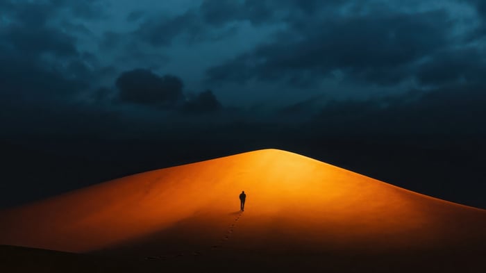 Silhouette of a person walking on a sand dune at dusk