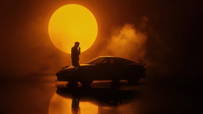 Man leaning on a car with a large sun behind